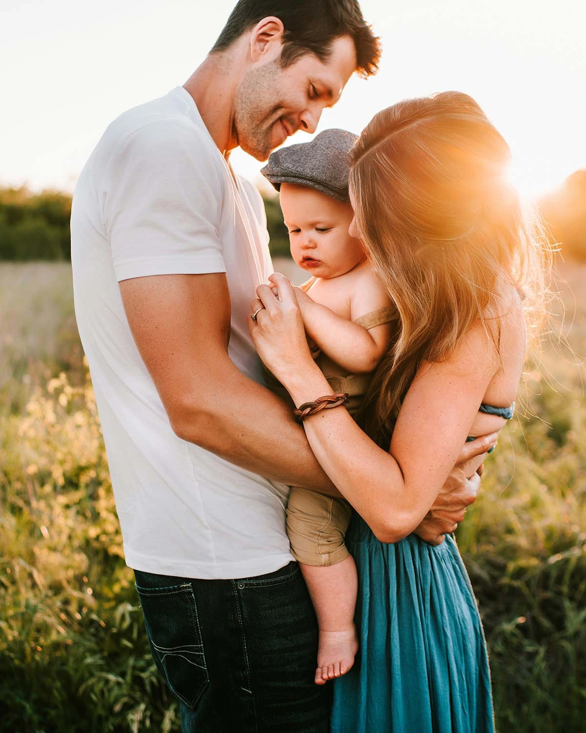 A family of four smiling together in a sunny field, surrounded by tall grass and wildflowers